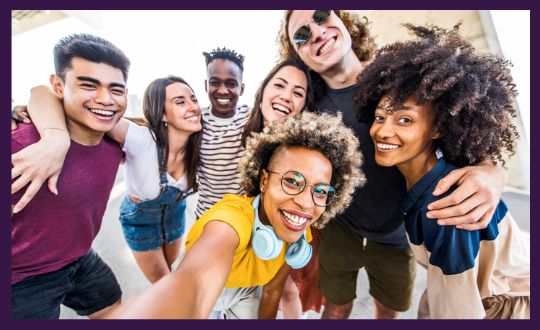 A diverse group of young adults joyfully posing together for a selfie, featuring smiles and a vibrant atmosphere.